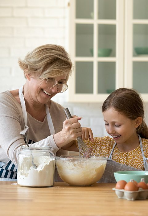 Grand-mère fait et sa petite-fille dans la cuisine pour illustrer la page de l'épargne-pension en branche 23 de DVV