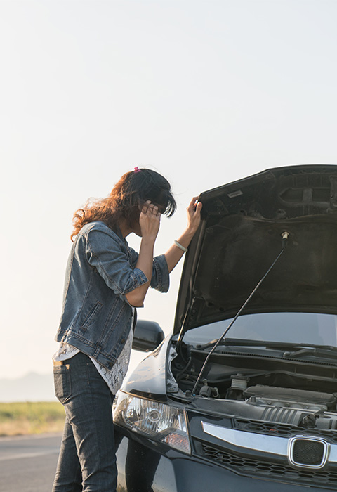 Vrouw met autopech die onder de open motorkap kijkt als illustratie voor de pagina optie voertuigbjstand van DVV 