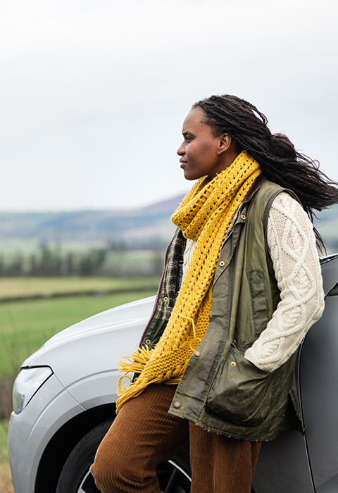 Jonge vrouw voor haar auto genietend van het leven als illustratie voor de pagina van de verzekeringen voor de auto bij DVV.