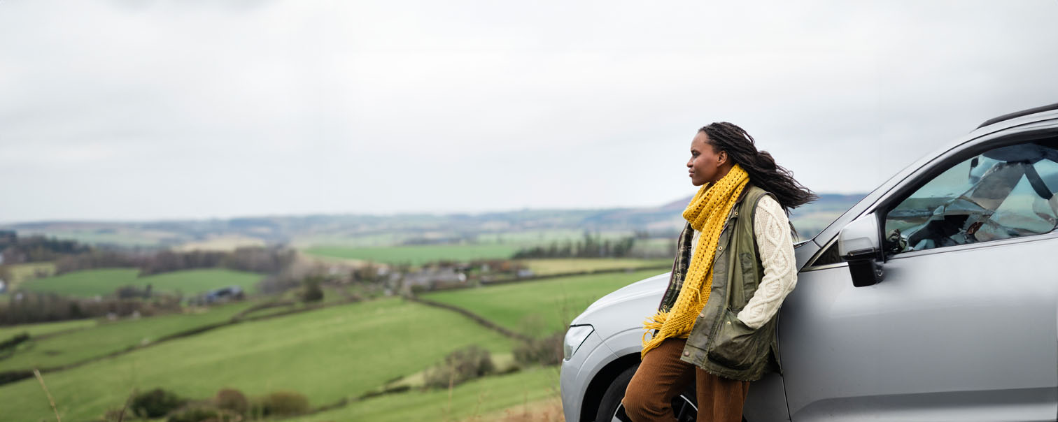Jonge vrouw voor haar auto genietend van het leven als illustratie voor de pagina van de verzekeringen voor de auto bij DVV.