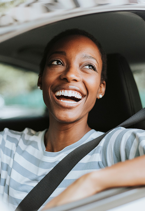 Jonge vrouw in haar auto die lacht als illustratie voor de pagina autoverzekering van DVV