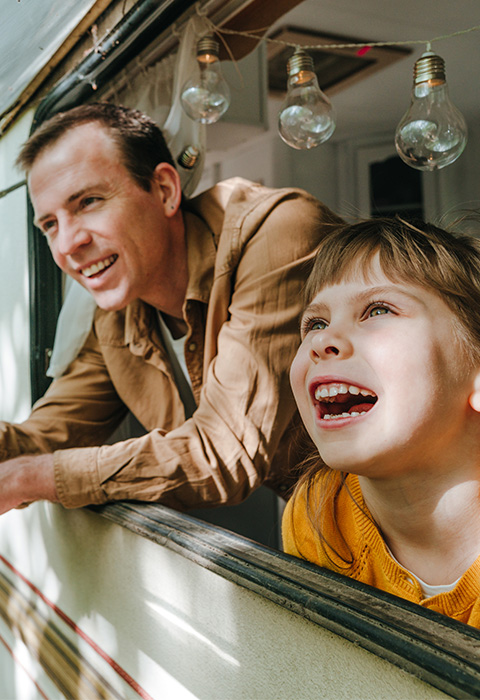 Papa en dochter die uit het raampje van de mobilhome kijken als illustratie voor de pagina camperverzekering van DVV 