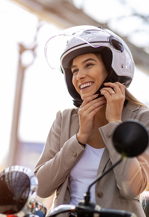 Vrouw op een scooter die  helm aandoet als illustratie voor de pagina van de moto- en scooterverzekeringen van DVV 