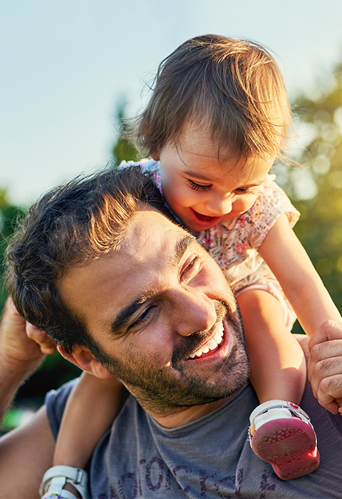 Des parents dont papa avec un bébé sur les épaules pour illustrer la page de l'assurance familiale de DVV