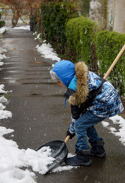 Petit garçon dégageant la neige du trottoir pour illustrer la page comparative des protections juridique dans le cadre privé