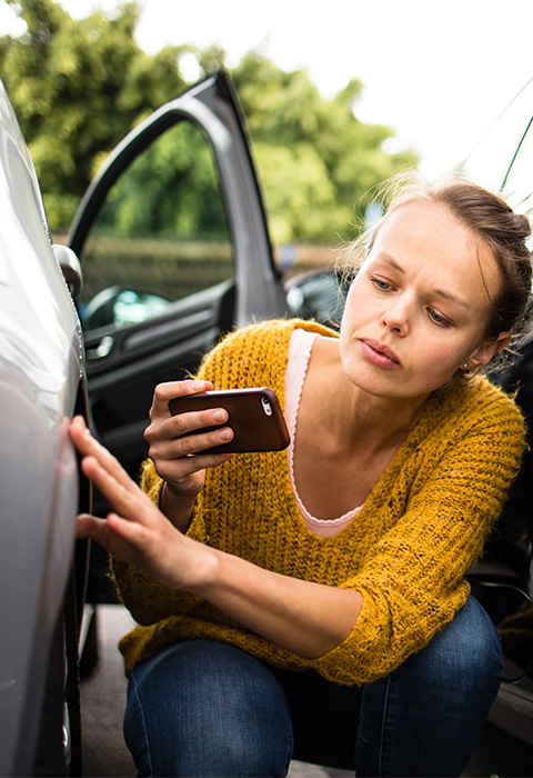 Jeune femmme inspectant deux voitures après un accident pour illustrer la page comparative de protection juridique auto