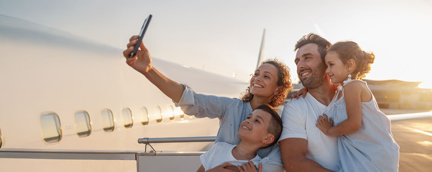 Gezinnetje neemt een selfie op de trap van het vliegtuig als illustratie voor de pagina van de reisbijstand van DVV 