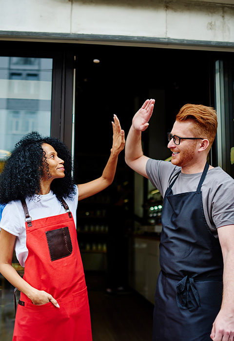 Twee collega's geven elkaar high five als illustratie voor de pagina van aansprakelijkheidsverzekeringen voor zelfstandigen en kleine ondernemingen 