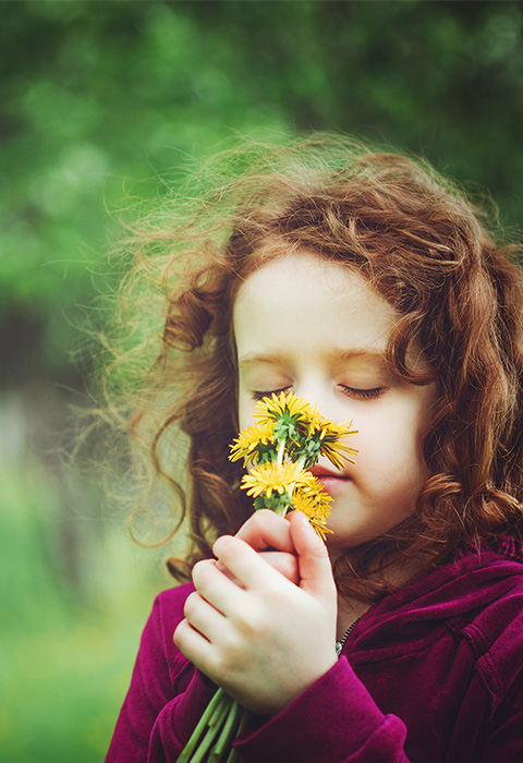 Kindje dat aan bloemen ruikt als illustratie van de pagina overlijdensdekking van verschillende pensioenverzekeringen van DVV 