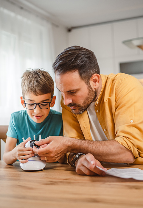 Vader en zoon die een nieuw voorwerp ontdekken als illustratie van de dekking premievrijstelling van verschillende pensioenverzekeringen 